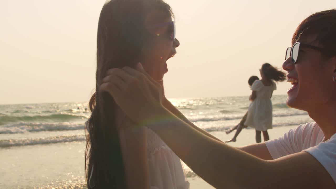 아빠가 아이를 돕고 선글라스를 착용하면서 해가 지면 바다 근처에서 함께 휴식을 취합니다. 느린 동작 촬영.