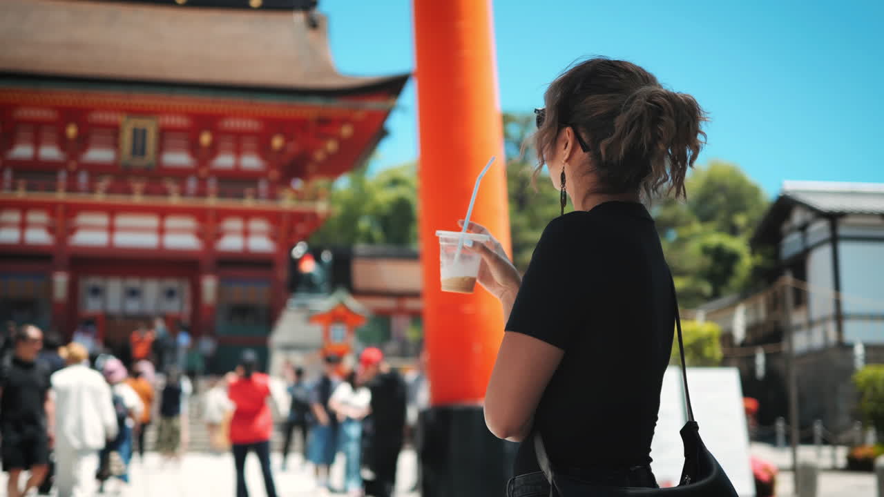 mujer bebiendo una bebida con una paja frente a una puerta roja del templo