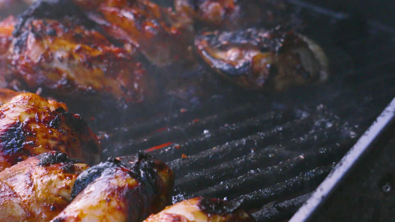 Chef Tongs Grabbing Juicy Soft Chicken Thigh from Smoking Hot BBQ with Flames Licking Meat from Below. Full Barbecue with Sausages Drumsticks. Outdoor Summer Cooking Food. Delcious and Tasty.