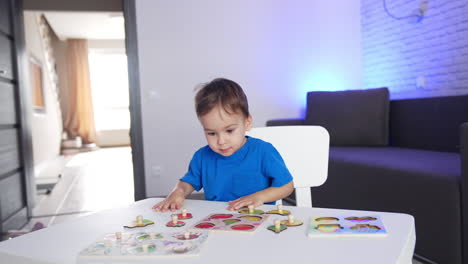 little kid in blue t-shirt runs up to a desk. lovely toddler sits down to play a game of puzzles.