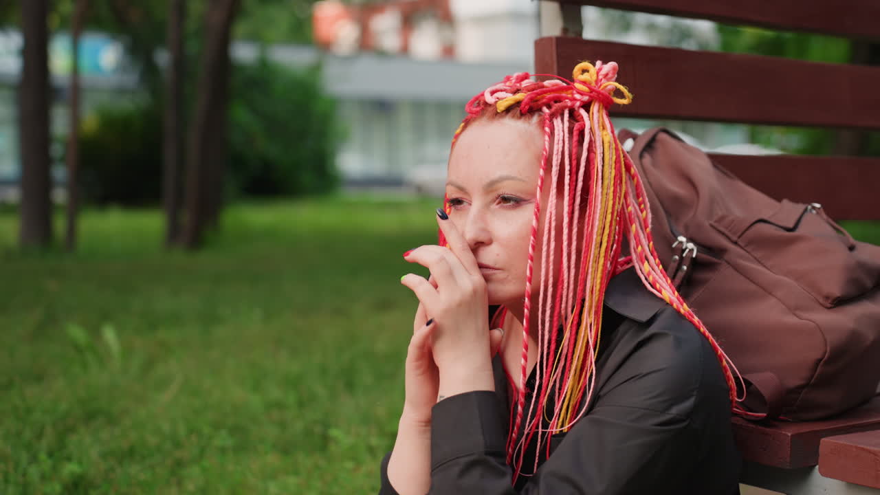 여성이 공원 벤치에 앉아 조용히 휴식을 취하고 있어요. 밝은 땋은 머리를 한 소녀가 공원에서 생각에 잠겨 앉아 있고, 화려한 머리를 한 여성이 활기찬 야외 환경 속 벤치에서 평화롭게 잠시 멈춰 있어요.