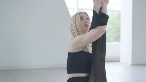 fit girl in black clothes performing contemporary. female dancer shows flowing motions, body and hands waves at white room. modern ballet dance choreography. young woman is moving smoothly