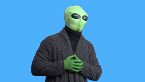 man in alien costume, warm knitted jacket, with funny themed mug in his hand laughs, writhes with laughter, against a blue chroma key. preparation for halloween party