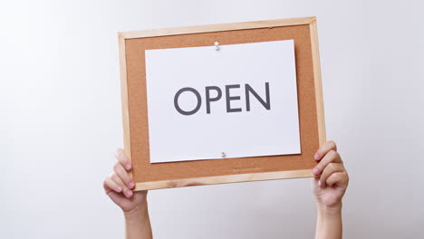 woman's hand shows the paper on board with the word open in white studio background with copy space