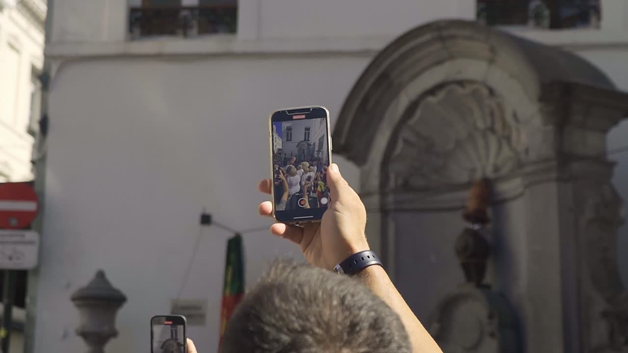 Male tourist taking a video of the statue of Manneke Pis in Brussels (costume change).