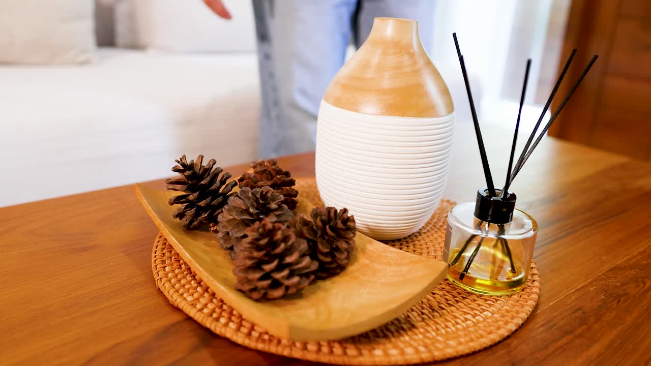 Mains de femme asiatique arrangeant un diffuseur d'huiles essentielles et des pommes de pin sur une table en bois.