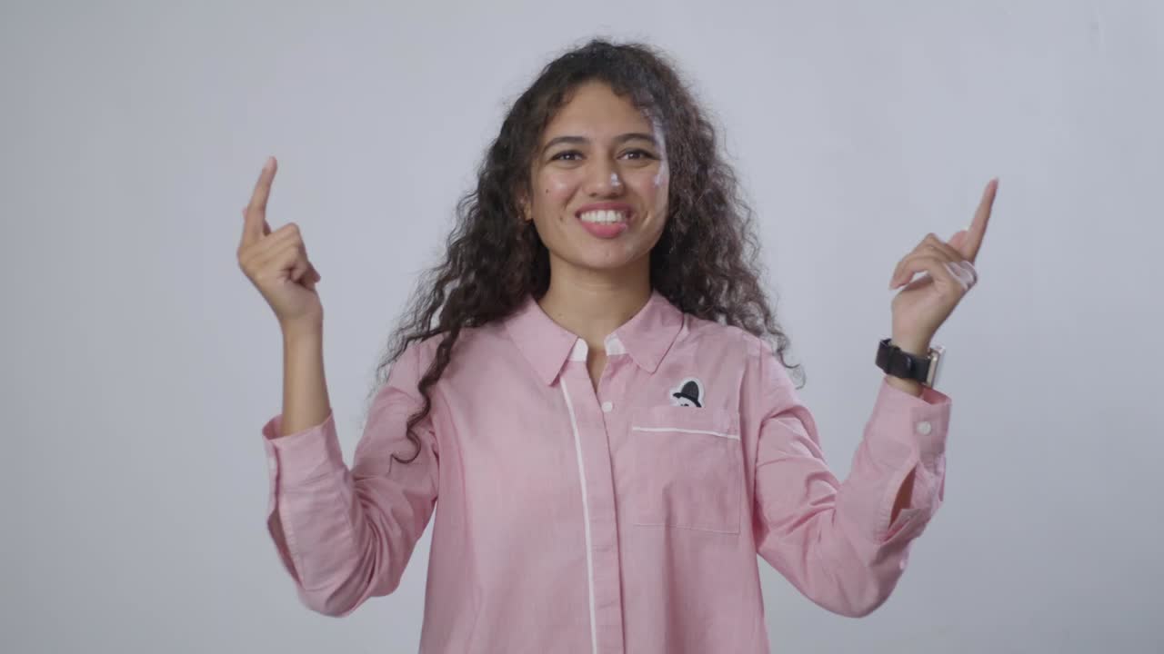 A South Asian woman with brown, curly hair presses her fingertips together, looking thoughtful and concerned