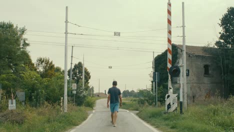 level crossing, a man dressed in light blue and blue walks and crosses it, filmed from behind