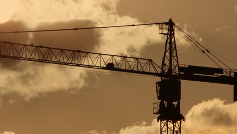 silhouette tower crane works at construction site. high-rise crane with jib rotates on background of sunset sky with clouds