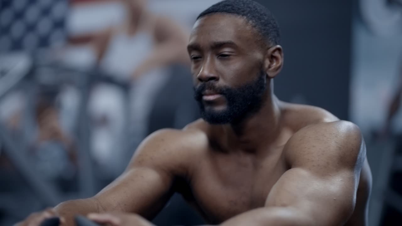 Muscular African American man performs Seated cable rows in gym