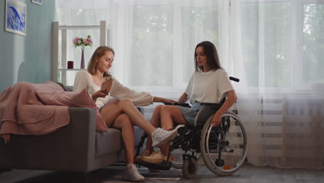 blonde woman helps disabled girlfriend to move in wheelchair