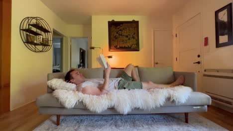 a caucasian reading a book on a white fur-covered couch