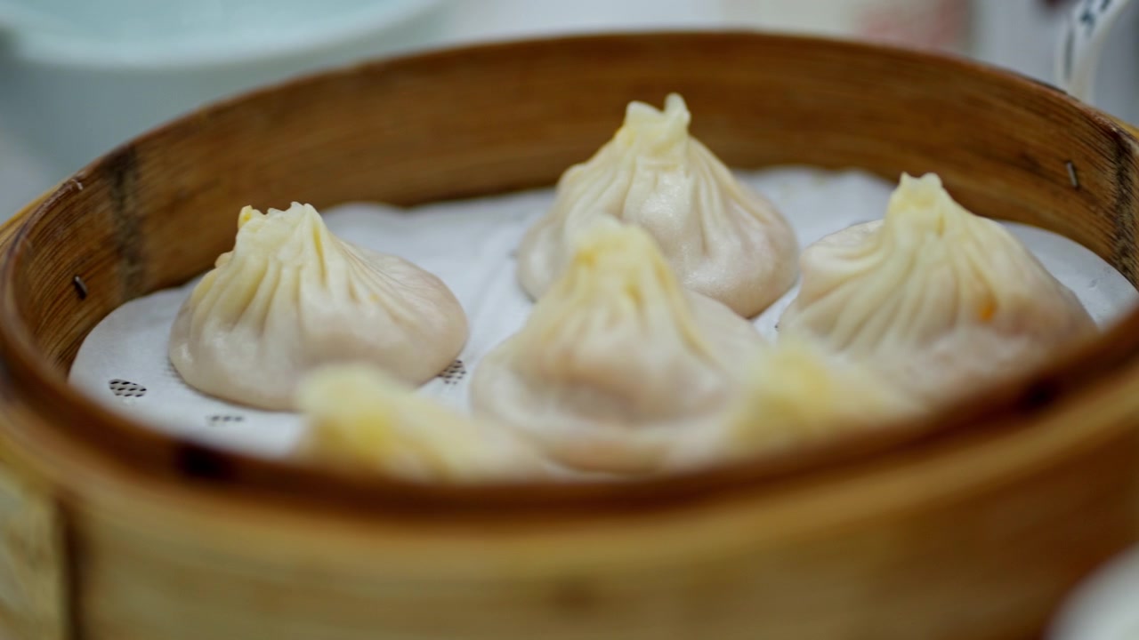 Tampilan dekat pangsit xiao long bao yang baru dikukus dalam keranjang bambu. Ideal untuk fitur kuliner atau promosi masakan Asia