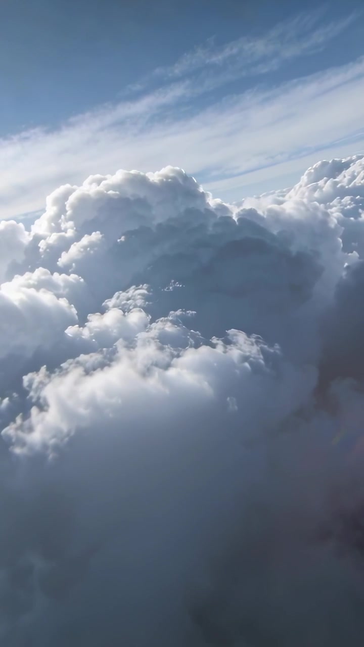 Video verticale: Telecamera che filma grandi cumuli mentre l'aereo raggiunge la quota di crociera, con cirri e cielo blu.