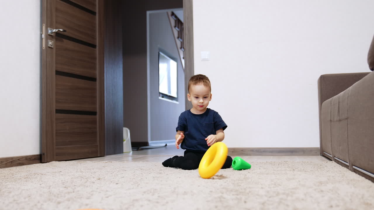 Two year old toddler playing with the details of toy pyramid. Kid sits on the carpet rolling the toy by the floor.