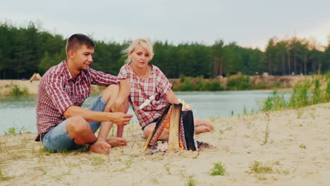 two friends are heated by the fire roast marshmallows on sticks against the backdrop of the river an