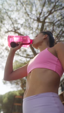 woman drinking water from a pink bottle outdoors
