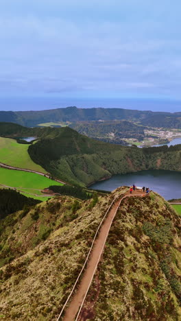 woman runs by the path leading to the top of the high mountain. small lake in the volcano crater at backdrop. the azores. top view. vertical video.