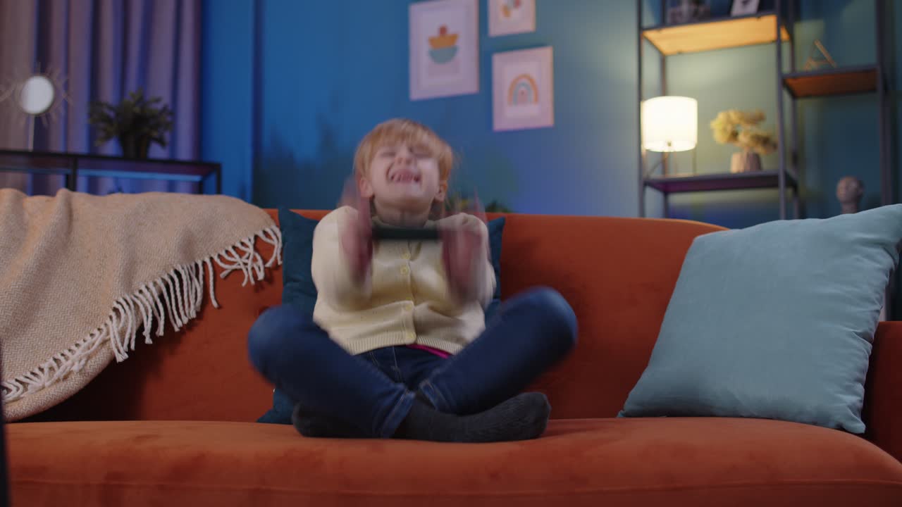 Worried child girl kid enthusiastically playing racing video games on mobile phone at home on sofa