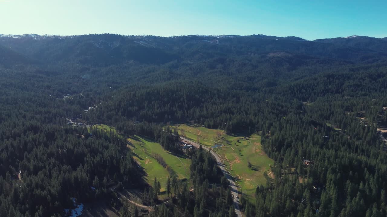 vista aérea del campo de golf rodeado de bosque de pinos y montañas