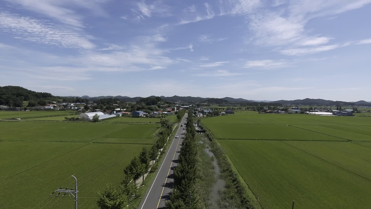 A motorway among rural landscape of rice farming area of Korea. Cars running on the road. Village far away