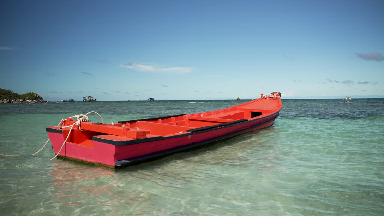 un barco de madera roja se sienta pacíficamente en aguas poco profundas de color turquesa, ofreciendo una vista serena del paraíso tropical