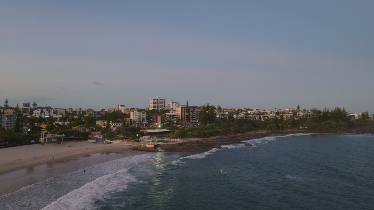 caída de la noche en la costa del sol ciudad costera avión no tripulado zoomando desde apartamentos con vista a la playa al océano, 4k australia