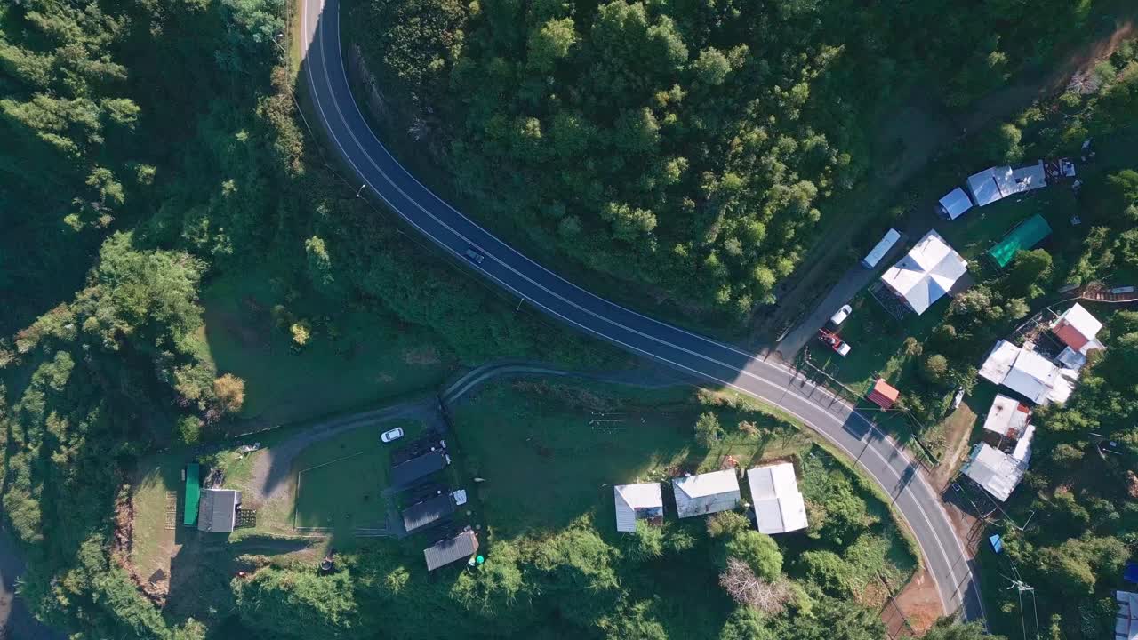 Spiral bird's eye drone aerial of village with scattered houses, colorful rooftops, winding roads, and dense green forest vegetation