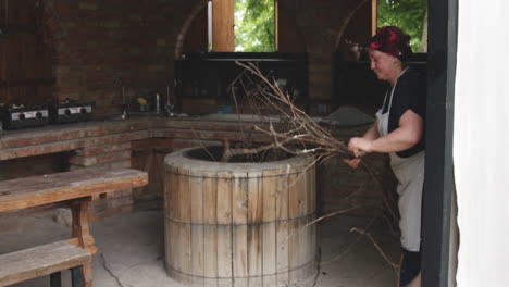 mujer panadera poniendo ramitas de madera dentro de un horno de barro redondo para hornear pan tradicional en kakheti, georgia