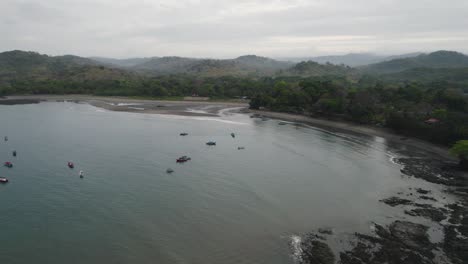 Boats-dot-the-calm-waters-of-Santa-Catalina,-Panama,-against-a-backdrop-of-lush-hills-and-a-rocky-shore