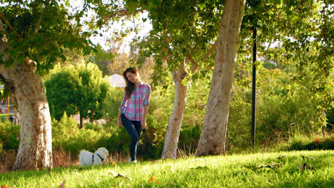 Mujer-Paseando-A-Un-Perro-Blanco-En-El-Parque-Hacia-La-Cámara