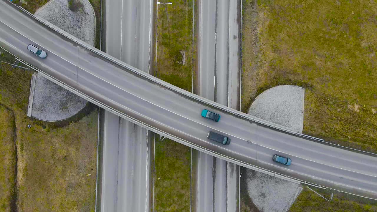 Top down aerial view ascending over a bridge or an overpass where cars, vehicles are driving over and under in Laagri Estonia during a cloudy day. The bridge is going over Tallinn Pärnu highway.