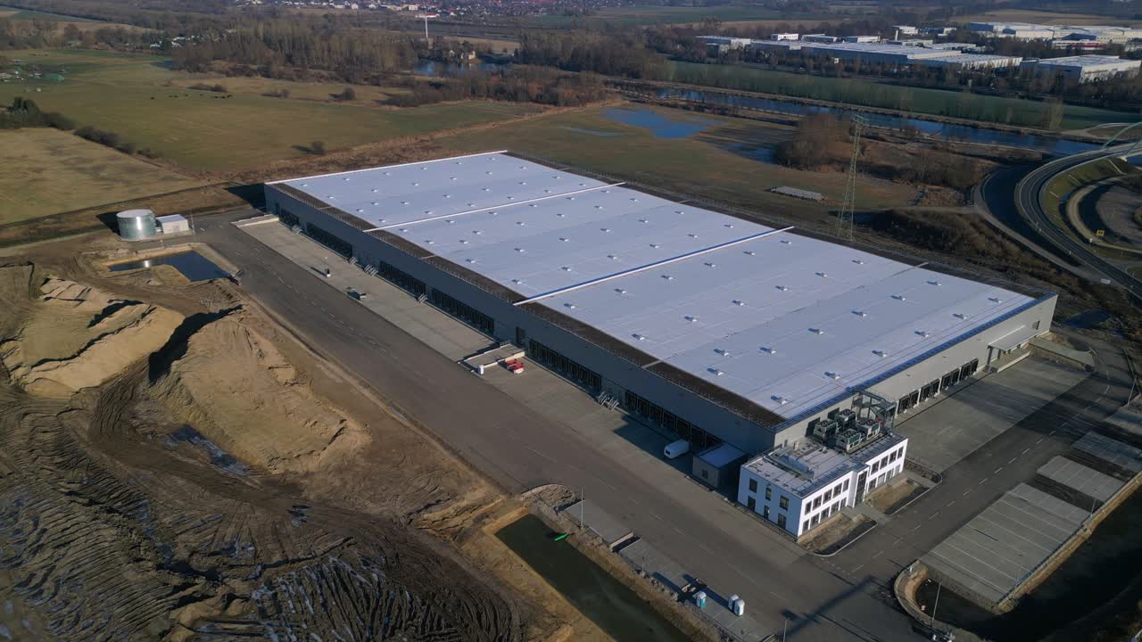 Nuovo grande edificio per un centro logistico in costruzione con un'ampia area di stoccaggio, banchine di carico e terreno circostante vuoto. Maestosa ripresa aerea con drone dall'alto