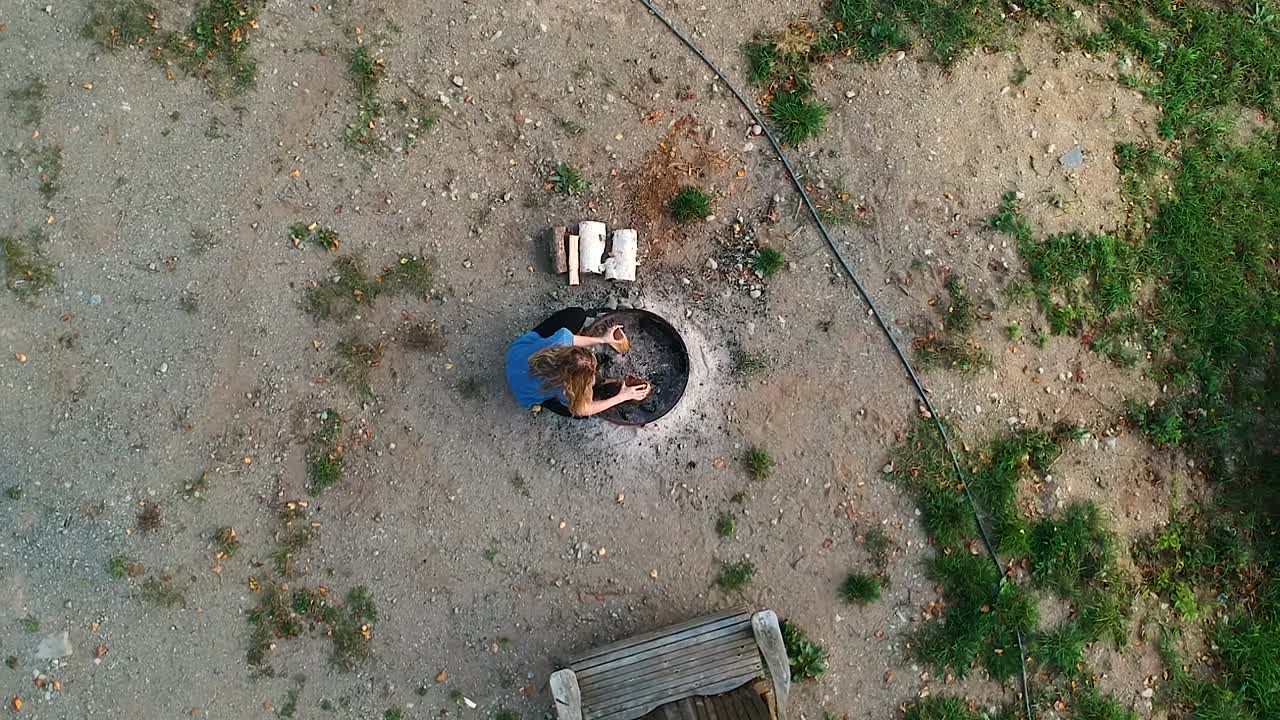 캐나다 온타리오 주 시골 공원에 있는 캠프장에서 화재를 준비하기 위해 화덕으로 걸어가 통나무를 천막에 쌓기 시작하는 젊은 여성의 독특한 조감도