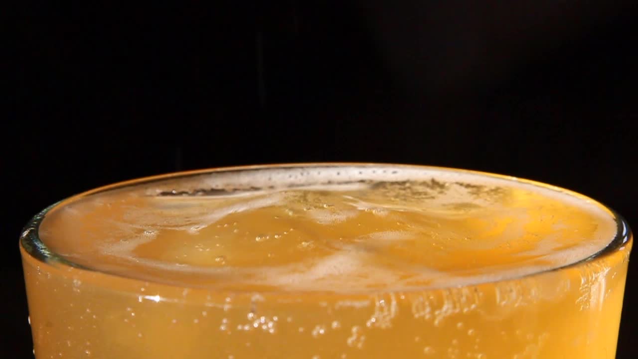 Un alto bicchiere di birra rinfrescante con le ultime goccioline di una mescita che increspano la superficie.