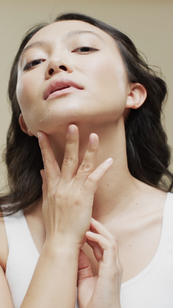 Vertical video of asian woman with dark hair on beige background, slow motion