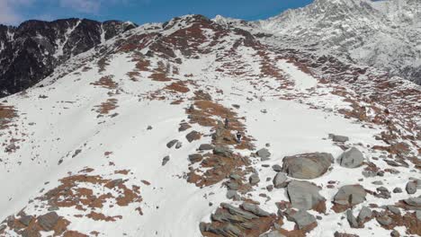 aerial dolly zoom-in shot of two people hiking to the top of triund peak with snow patches covered around them during the winters, shot with a drone in 4k