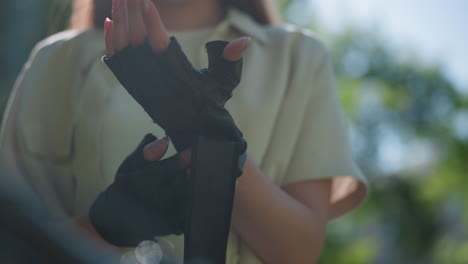 잔잔한 초록색을 배경으로 오토바이 장갑의 줄을 풀고 손가락에 초점을 맞추며 손가락을 부드럽게 조정하는 개인의 손의 클로즈업