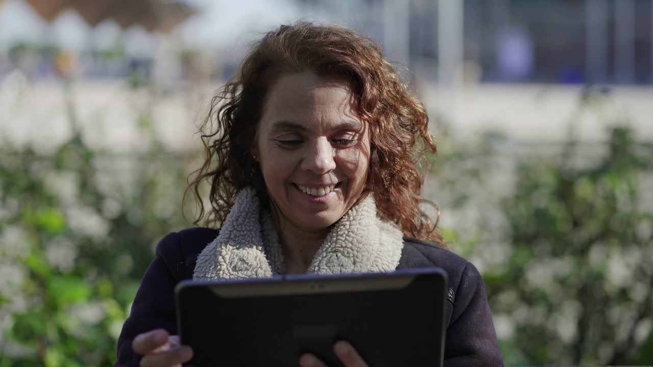 Smiling curly mature woman using tablet outdoor