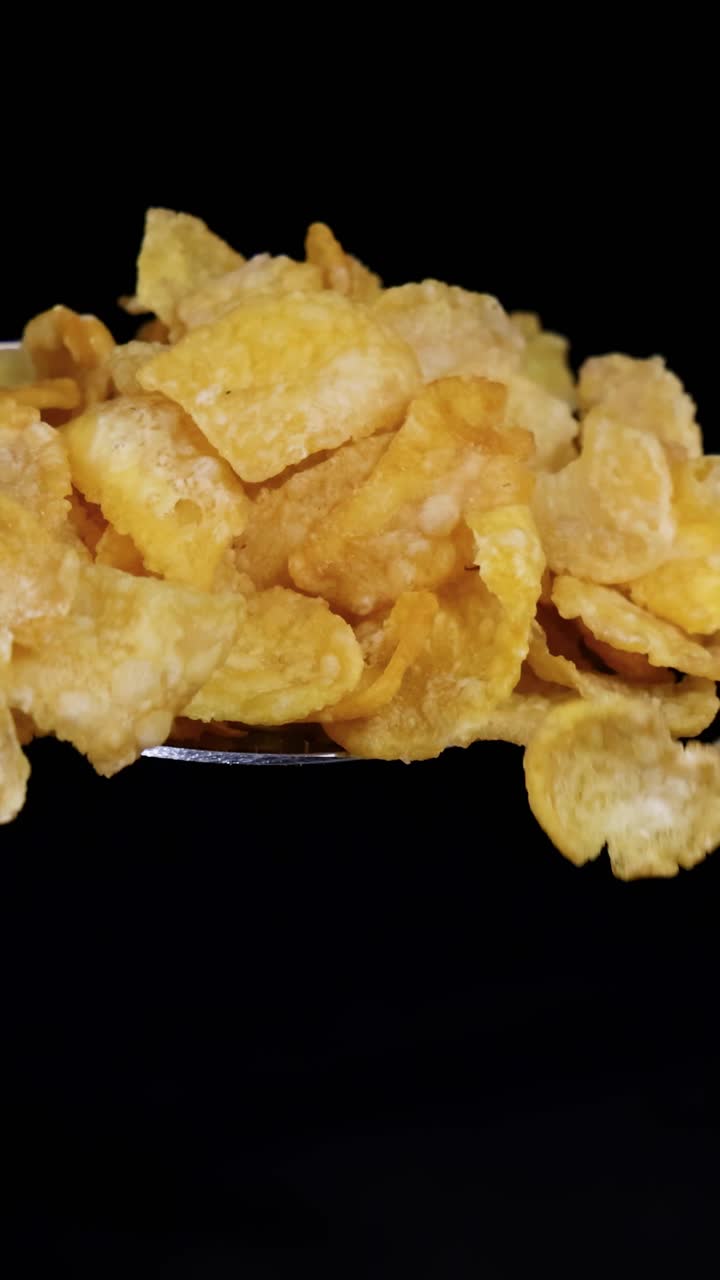 A spoon releases corn cereal flakes, falling gracefully against a dark backdrop, highlighting texture and motion