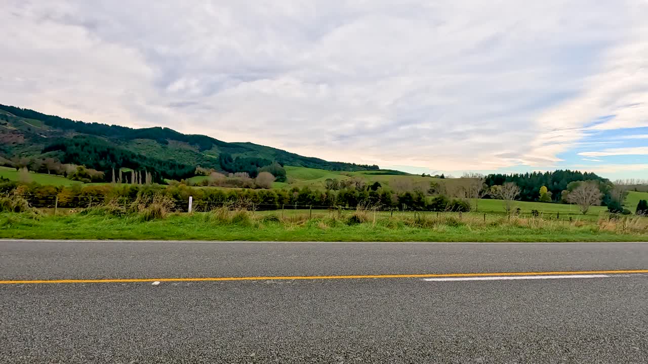 A tranquil road journey showcasing Lake Tekapo's lush hills under a cloudy sky, captured in natural daylight