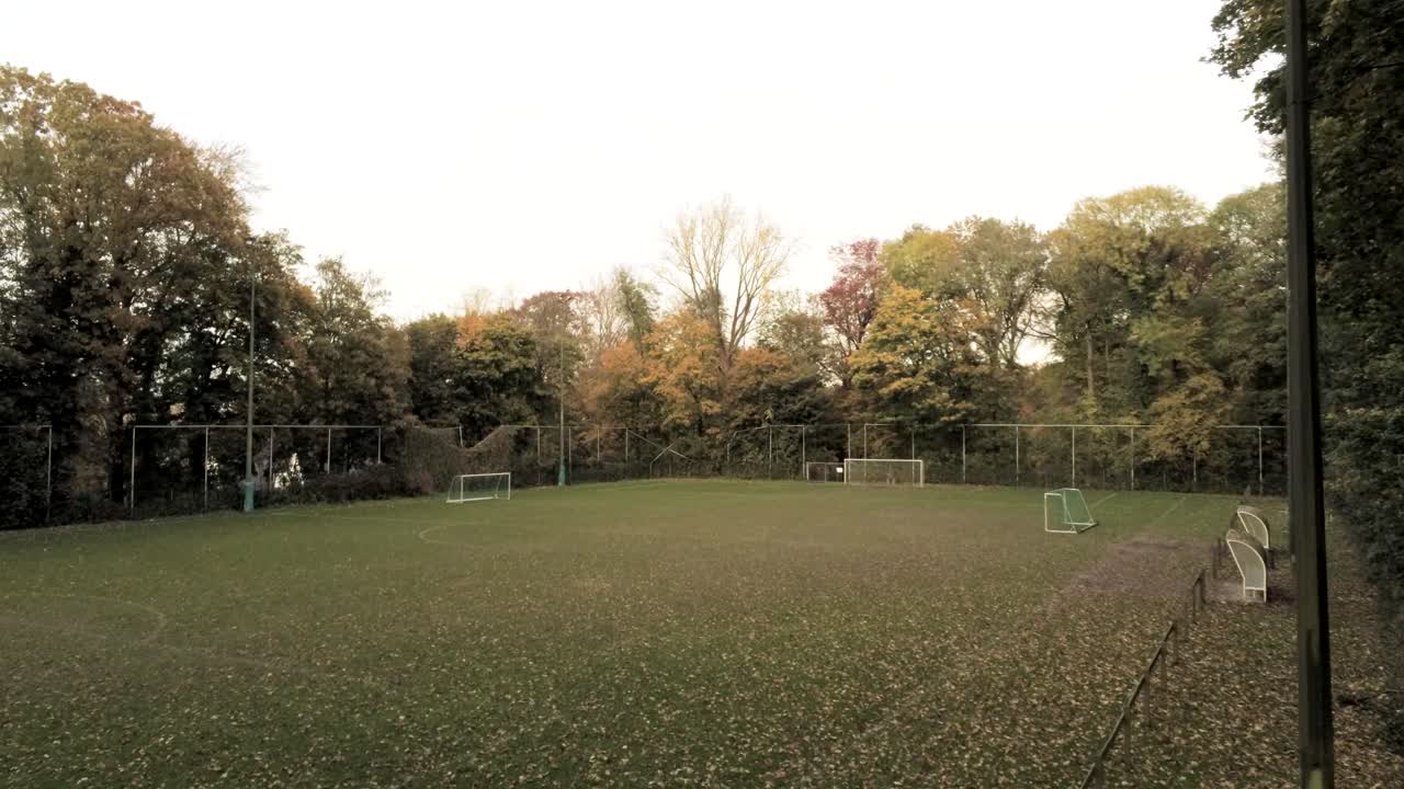 Flying through the broken fence of the soccer field in the middle of a lush hidden autumn forest - Aerial tracking shot
