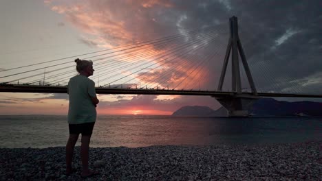 person watching sunset over the sea with a bridge in the background
