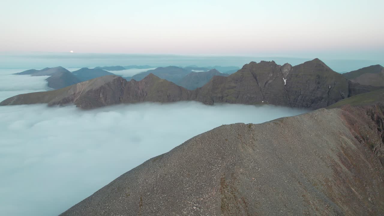 High mountain peaks surrounded by cloud inversion during sunset in Scotland. Drone panning shot