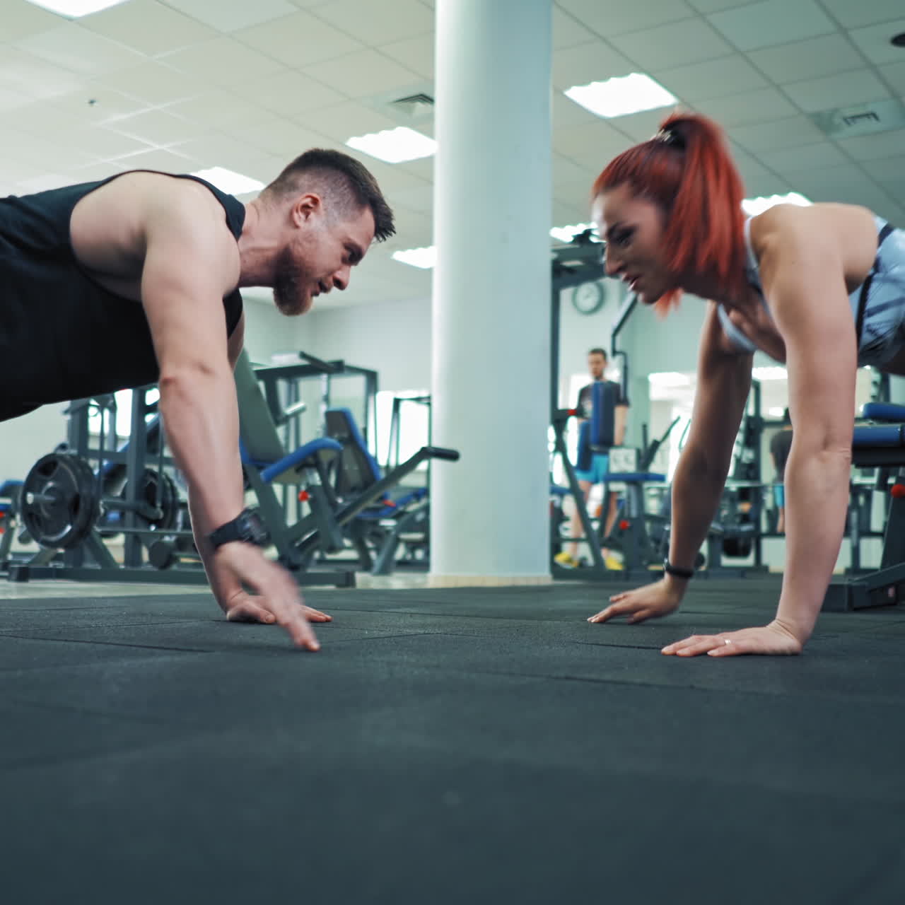 Muscular athletic man and beautiful fitness woman doing push ups exercise indoors. Healthy couple exercising on the floor one opposite other and giving five together in fitness center.