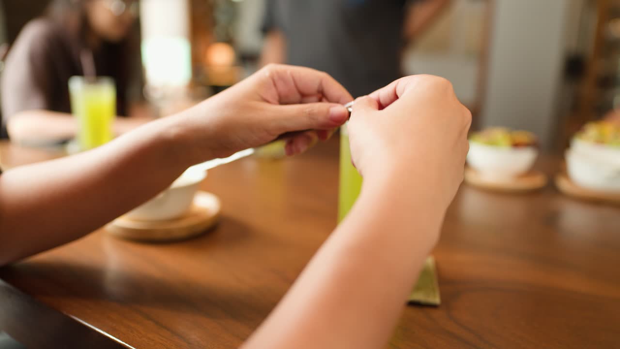 Person opens straw wrapper beside green drink at wooden restaurant table, natural lighting, close-up