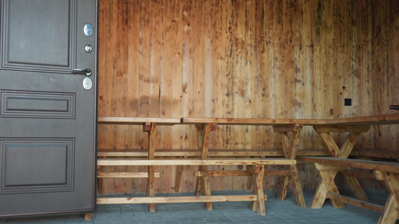 Open wood door leads into rustic resort seating area featuring long wooden benches against warm paneled walls and paved stone floor under covered entry