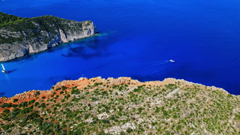 Luftaufnahme-Einer-Drohne-Vorwärts-über-Segelboote,-Die-An-Einem-Sonnigen-Tag-Den-Berühmten-Navagio-Strand-In-Griechenland-Erreichen,-Umgeben-Von-Hohen-Klippen