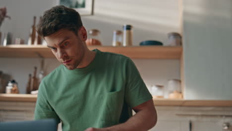 focused man pouring cornflakes at bowl in home closeup. brunette looking laptop