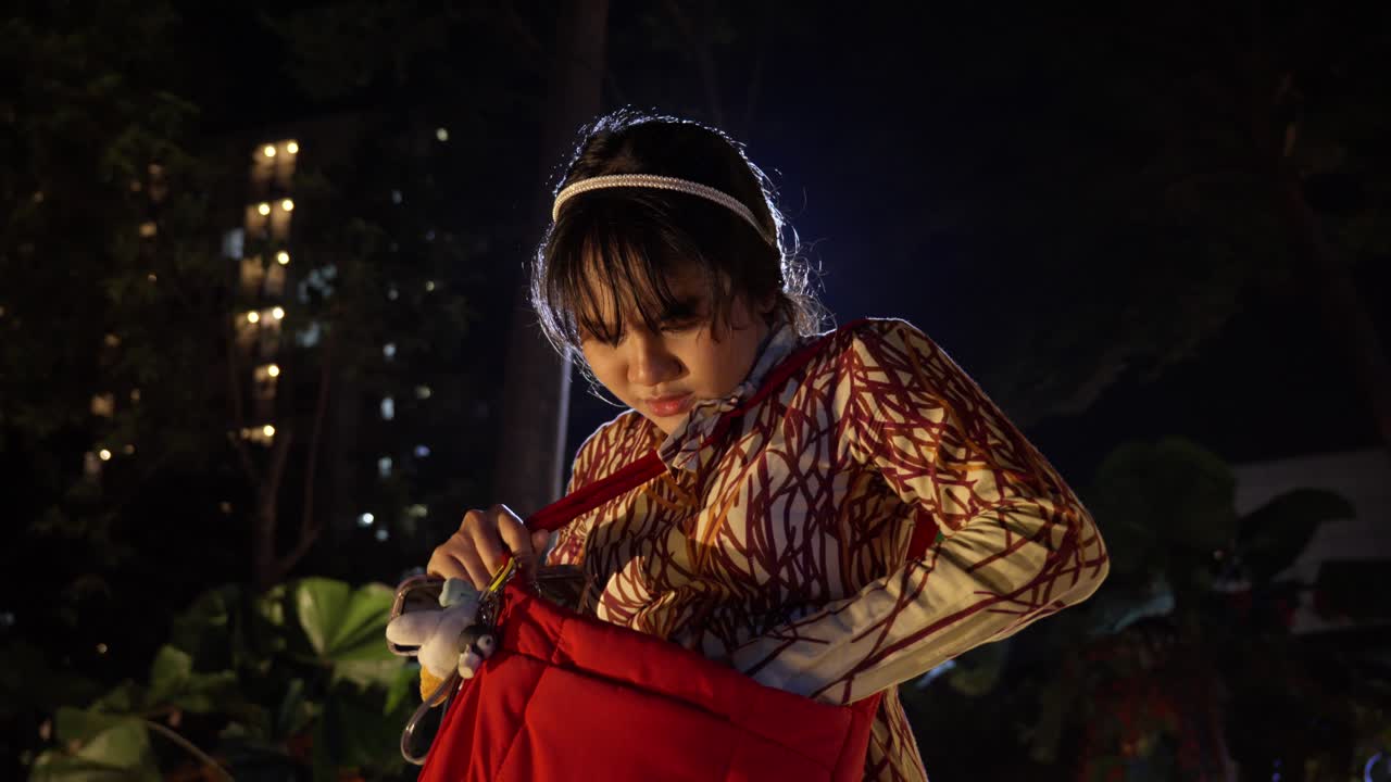 Young Woman Searching in Her Red Bag at Night